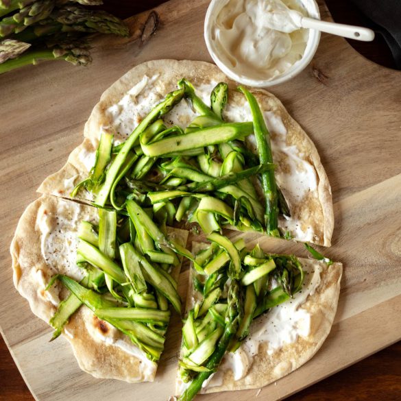 Flammkuchen mit grünem Spargel auf einem Holzbrett von oben fotografiert